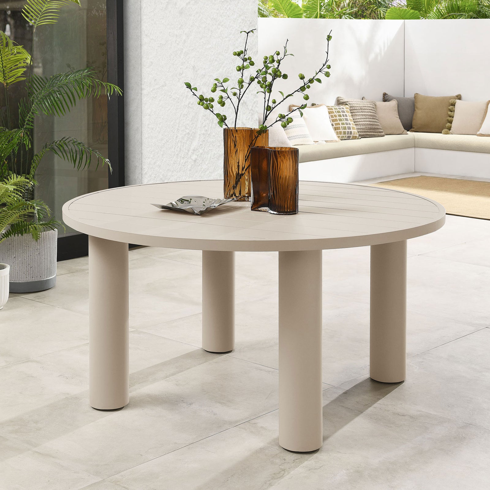 Taupe round aluminum dining table styled with amber glass vases and light chairs on a tranquil modern patio || EEI-6981-TAU || front_angle_room