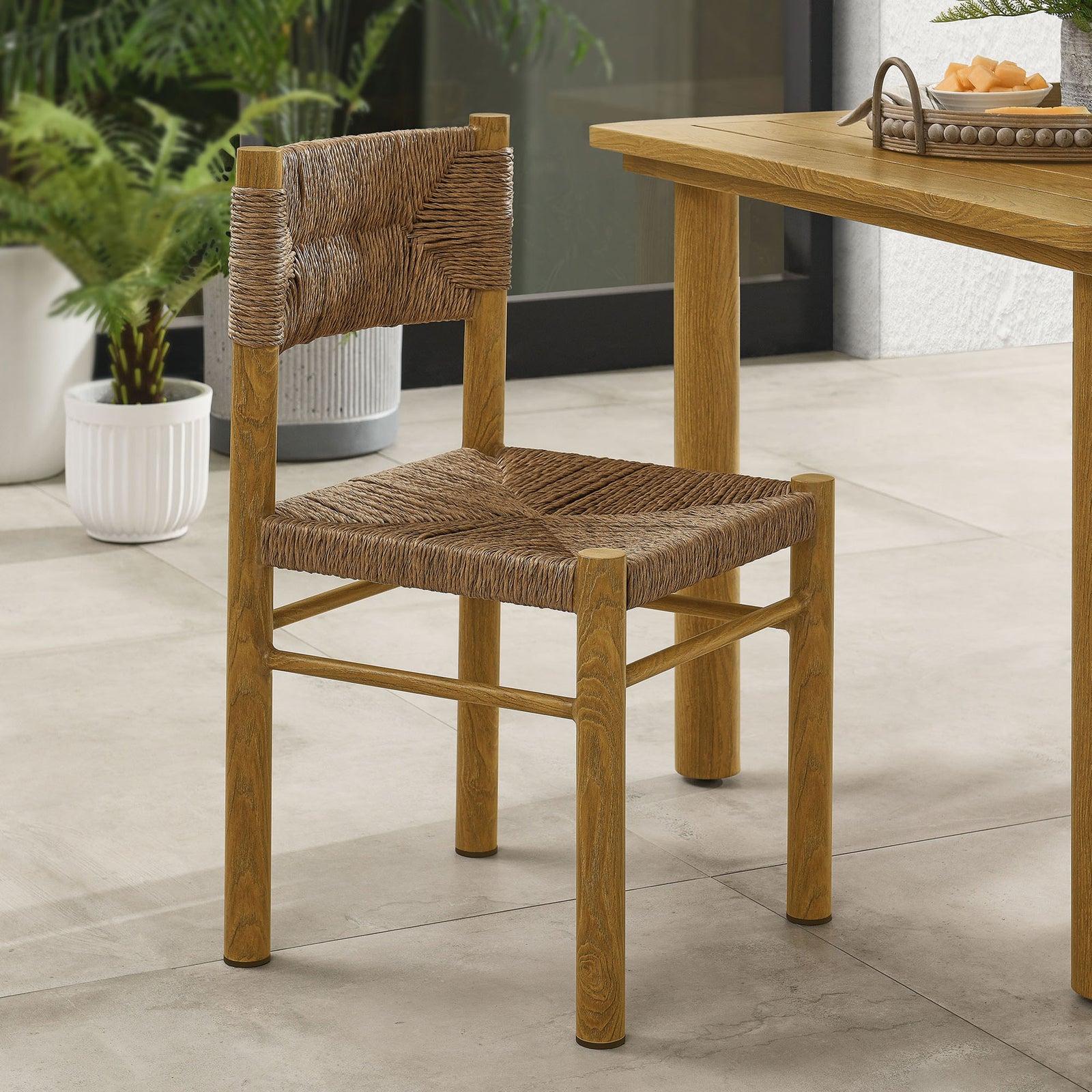 Natural rattan dining chair styled at an outdoor table with greenery, creating an inviting patio setting || EEI-6982-NAT || front_angle_room