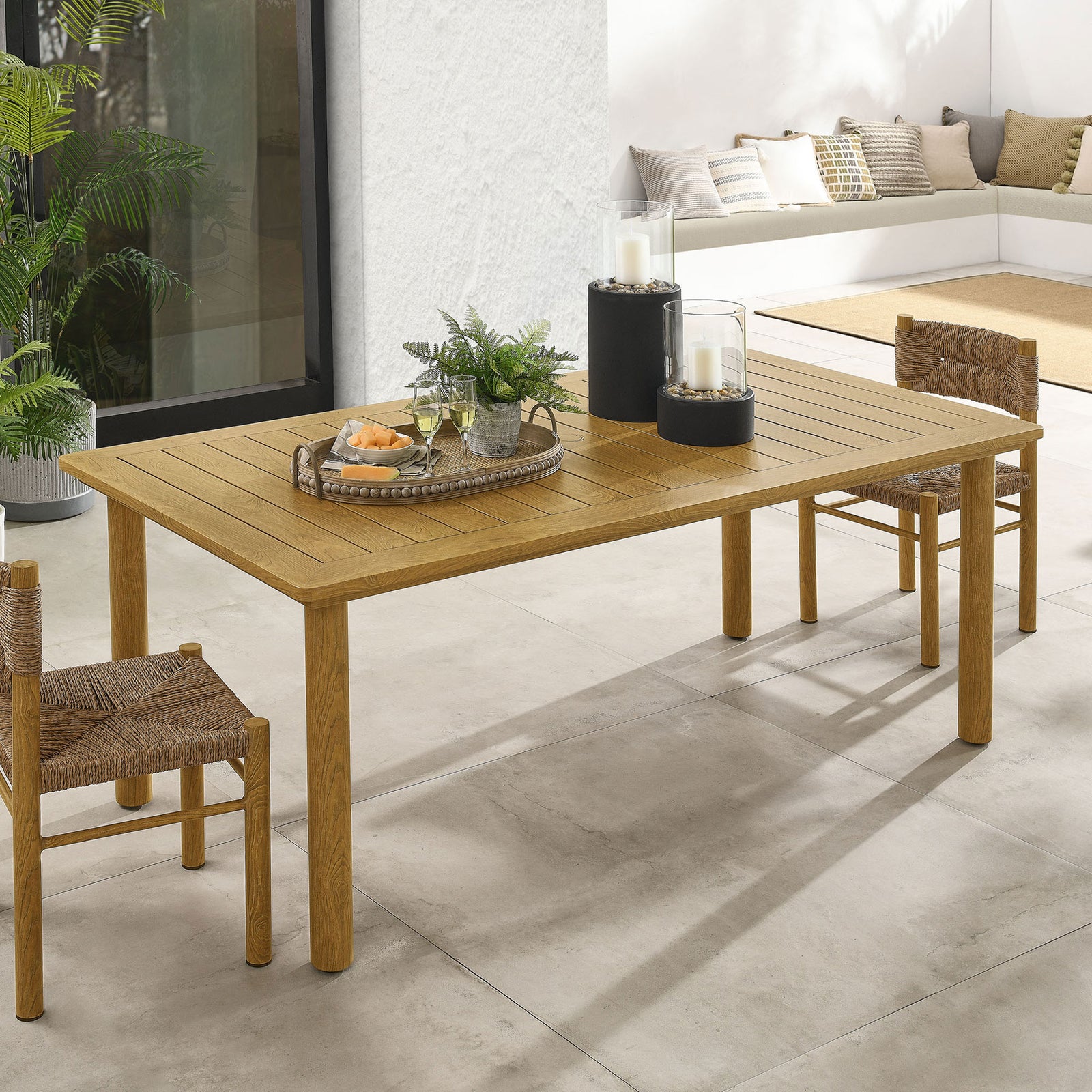 Natural slatted dining table styled with candles, greenery, and woven chairs in a bright patio setting || EEI-6985-NAT || top_angle_room