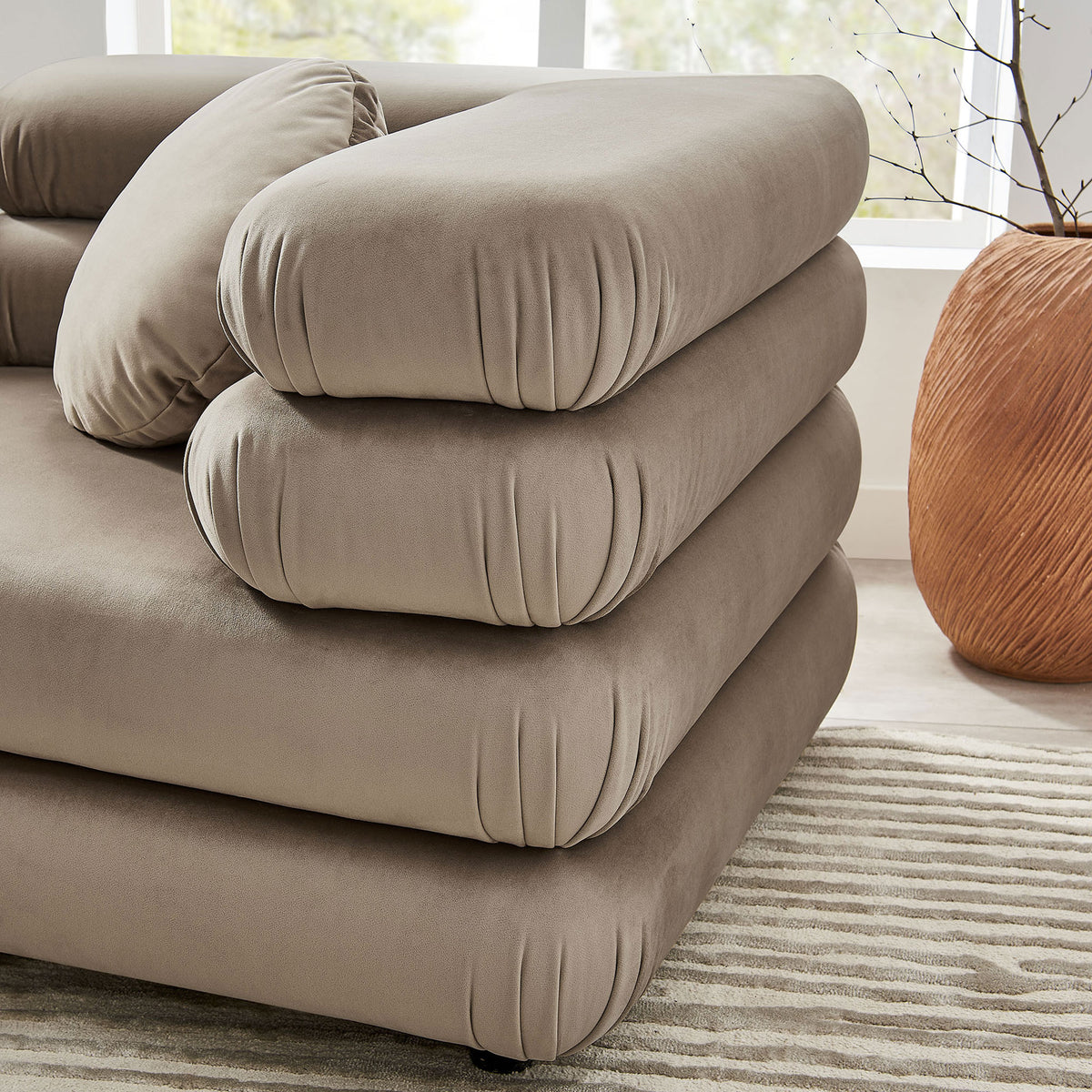Close view of Jubilee sectional arm showing layered taupe velvet cushions and round pillow detail on textured rug || EEI-7003-TAU || detail_room