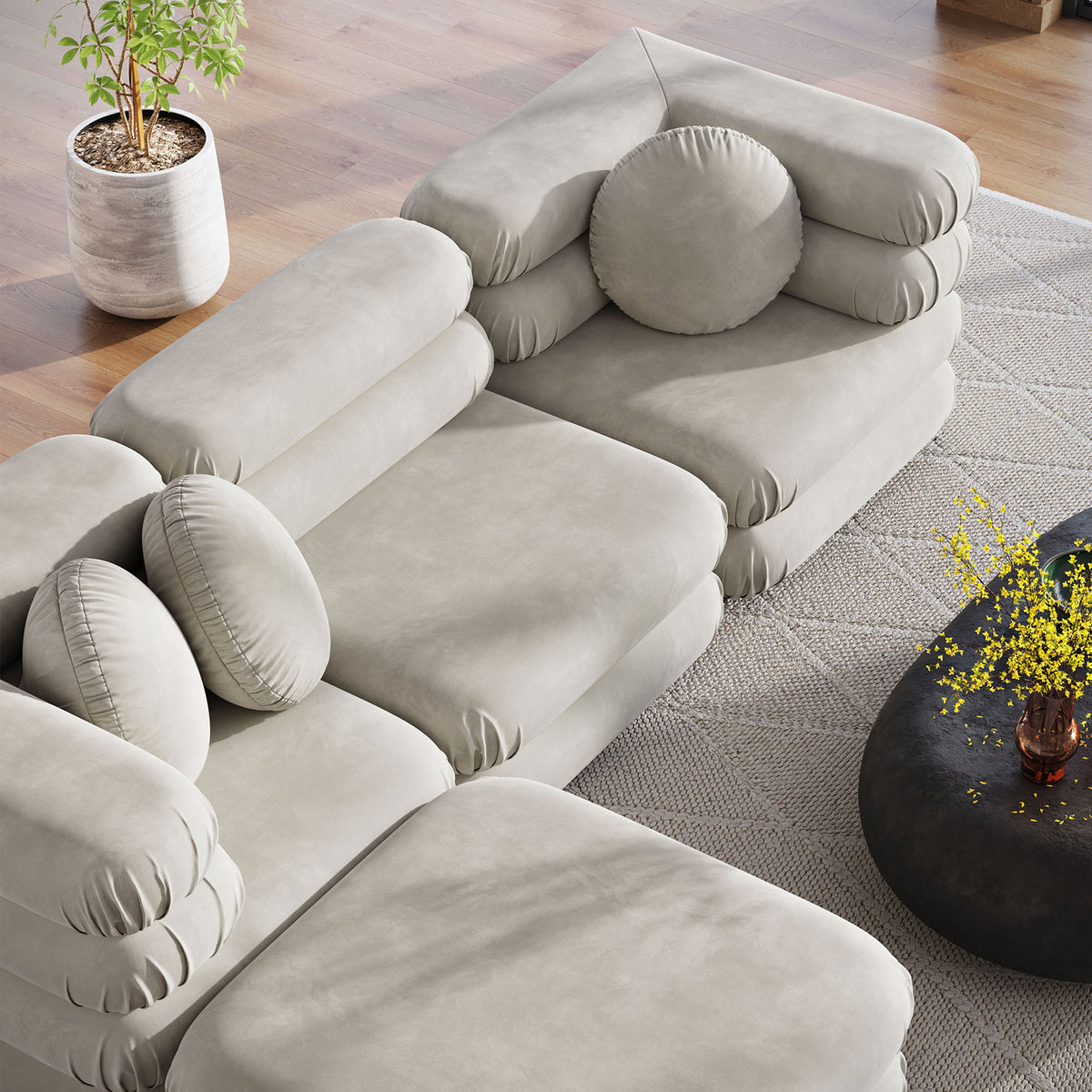 Almond modular sectional and ottoman surrounding a round coffee table, showcasing plush stacked cushions and pillows || EEI-7004-ALM || top_angle_room