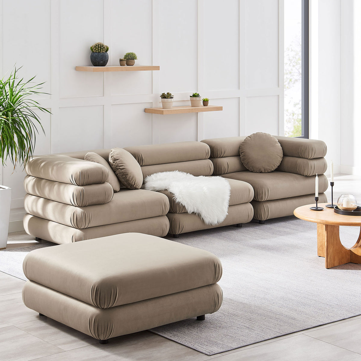 Taupe modular sectional with ottoman anchors a light living room with rug, plants, and wood table || EEI-7004-TAU || front_angle_room