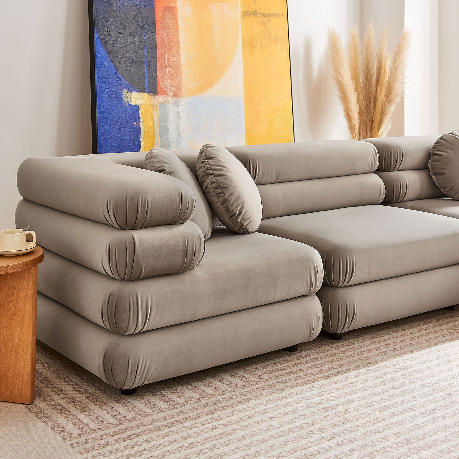 Taupe velvet sectional with rounded cushions styled with abstract art, pampas grass, and a neutral rug || EEI-7005-TAU || detail_room