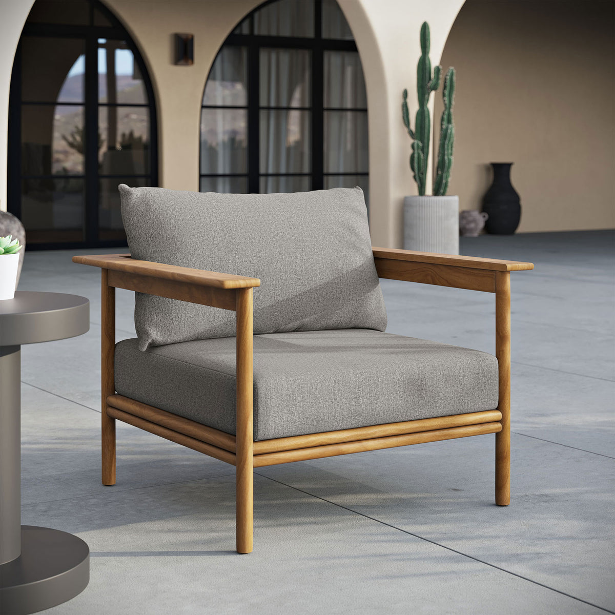 Light gray cushioned teak patio armchair set on a spacious outdoor terrace with arched architecture || EEI-7007-NAT-DRI || front_angle_room