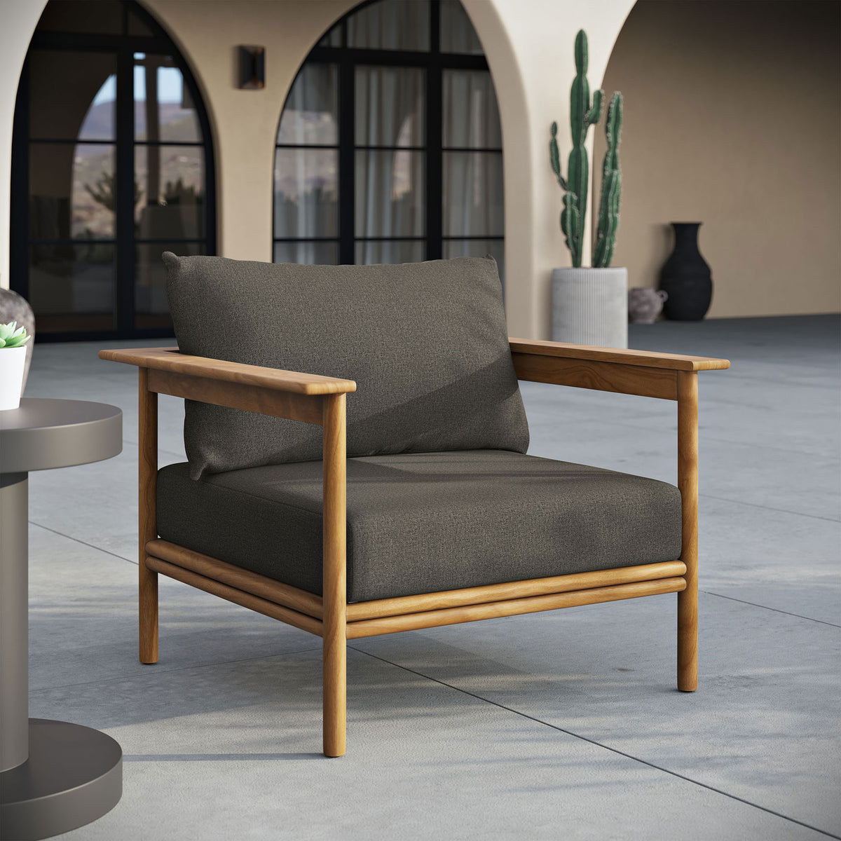 Charcoal cushioned teak patio armchair styled on a spacious terrace with arched outdoor architecture || EEI-7007-NAT-FLI || front_angle_room