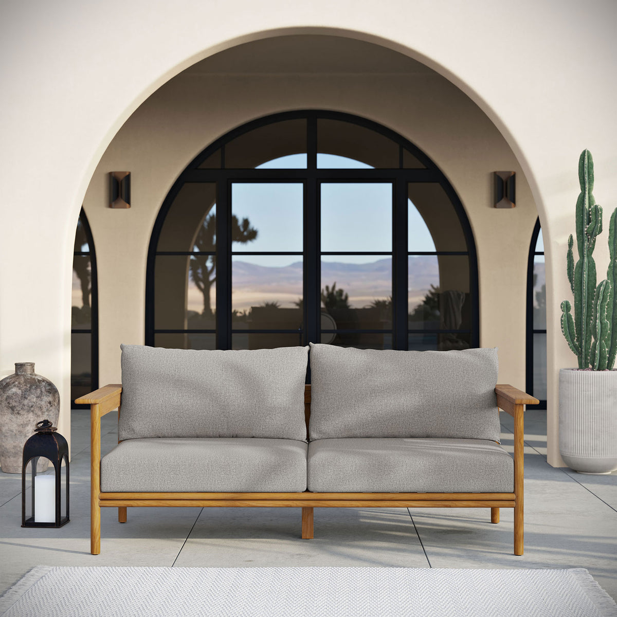 Teak outdoor sofa with gray cushions creating a relaxed focal point on a modern arched patio. || EEI-7008-NAT-DRI || front_room