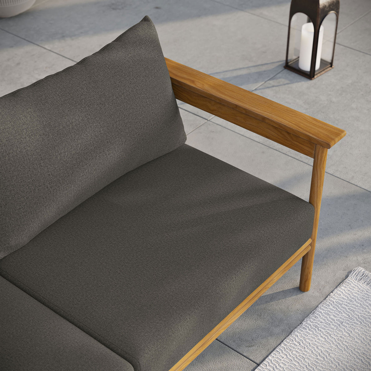 Charcoal outdoor sofa cushions and teak armrest styled with lantern decor on a sleek patio. || EEI-7008-NAT-FLI || detail_room