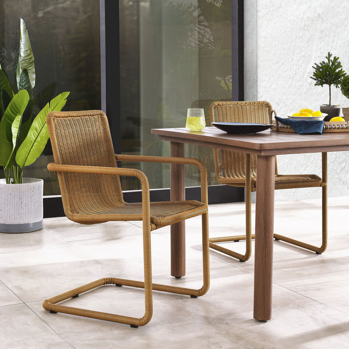 Natural wicker dining chairs styled on a patio beside a wood table with plants and sunlit flooring || EEI-7014-NAT || front_angle_multi_room