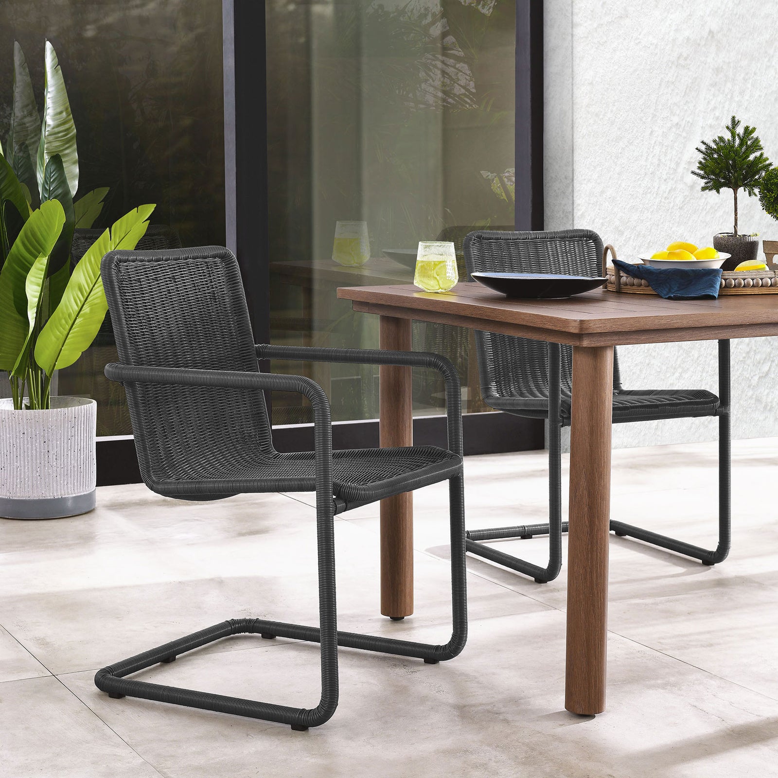Slate wicker chairs arranged around a wood dining table on a bright modern patio || EEI-7014-SLA || front_angle_multi_room