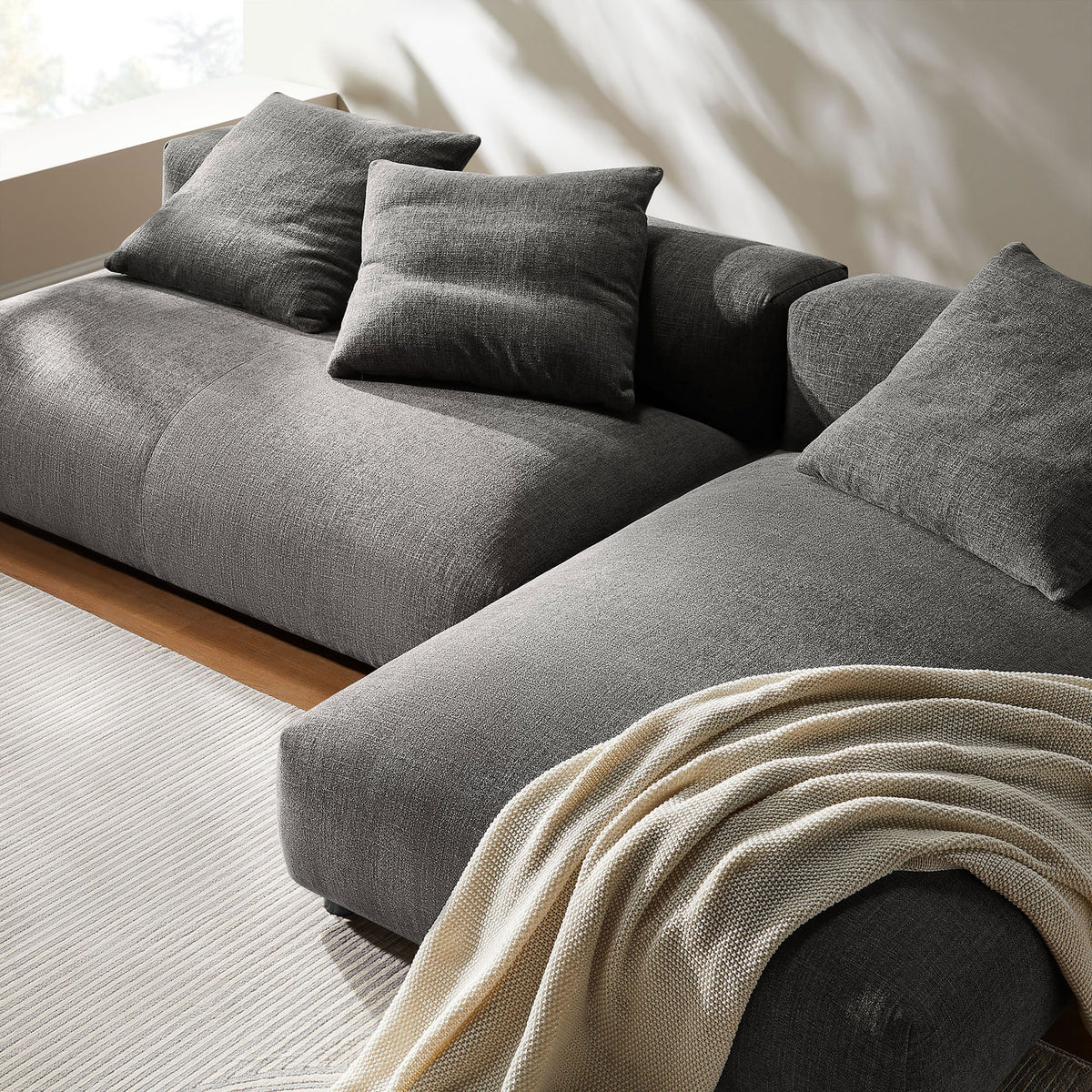 Charcoal chaise section with textured woven upholstery, plush cushions, and a soft throw for added warmth. || EEI-7025-CHA || detail_room