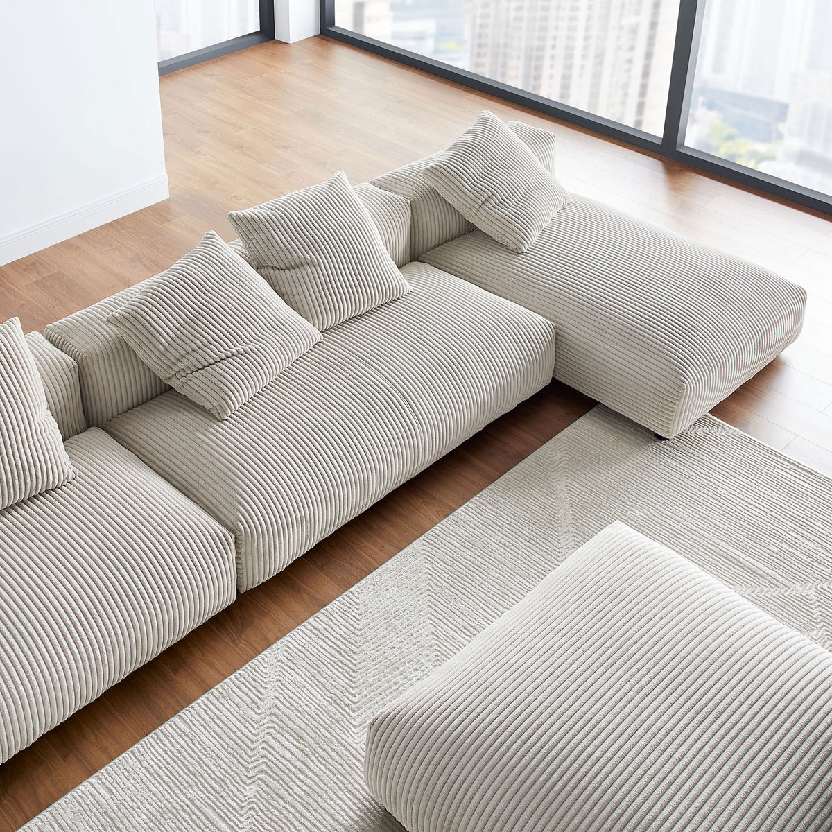 Generous L-shaped almond corduroy sectional with ottoman and pillows overlooking expansive floor-to-ceiling windows || EEI-7032-ALM || detail_room
