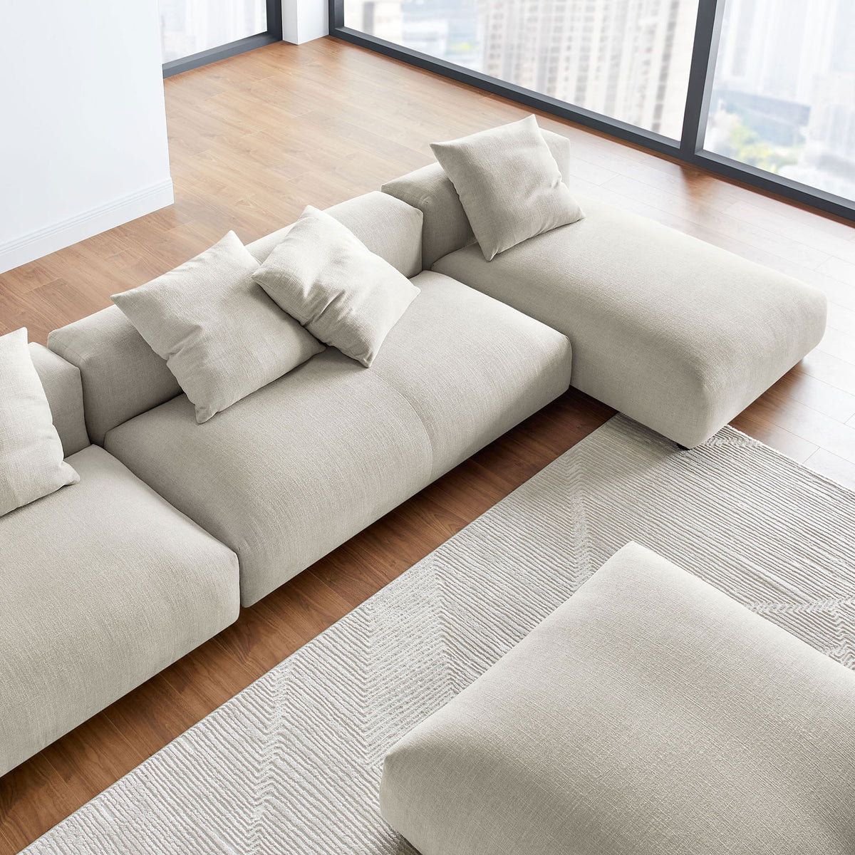 Linen modular sectional with chaise and ottoman arranged on layered rugs in a sunlit room || EEI-7033-LIN || detail_room