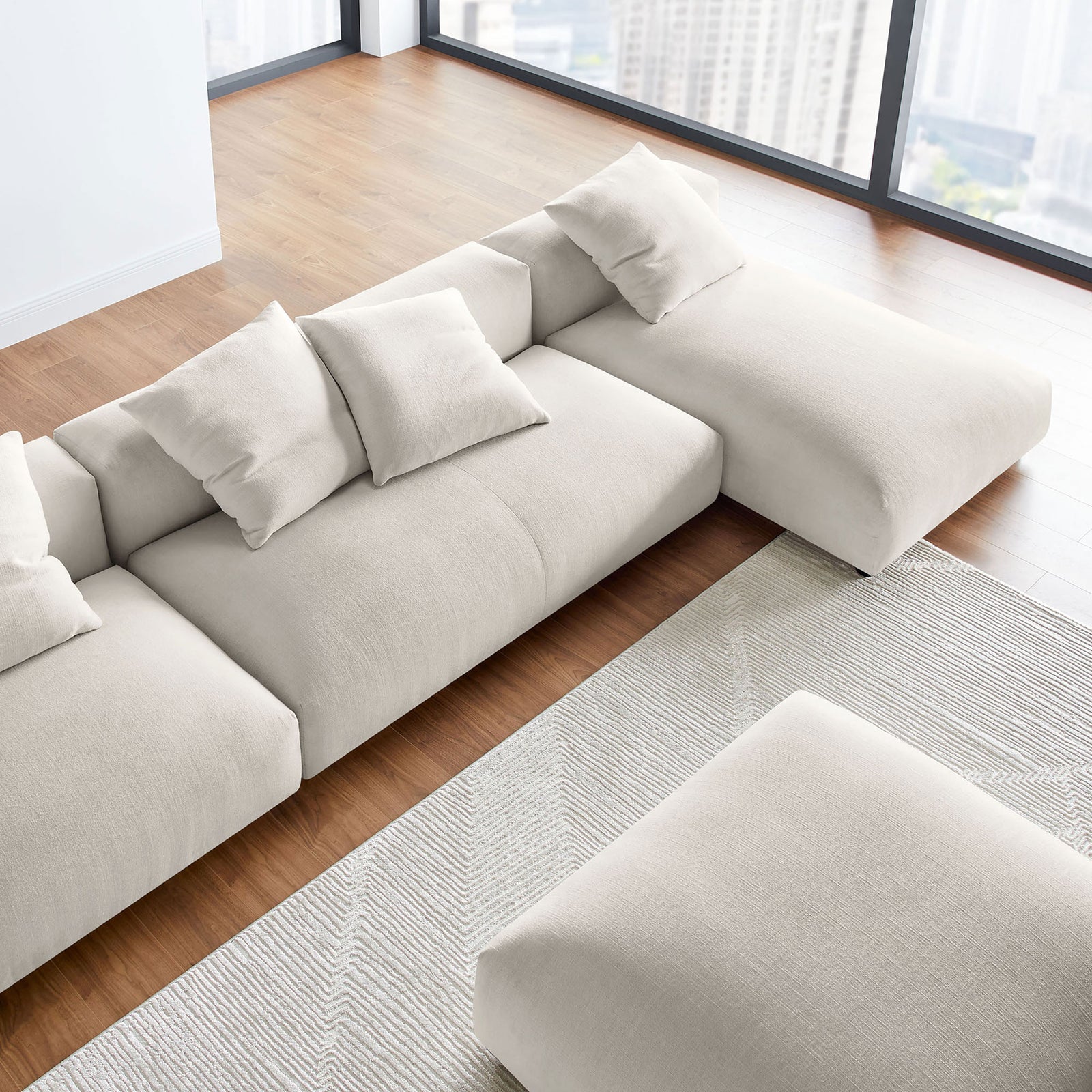 Modular salt fabric sectional with ottoman arranged in an airy living space with expansive floor to ceiling windows || EEI-7033-SAL || detail_room