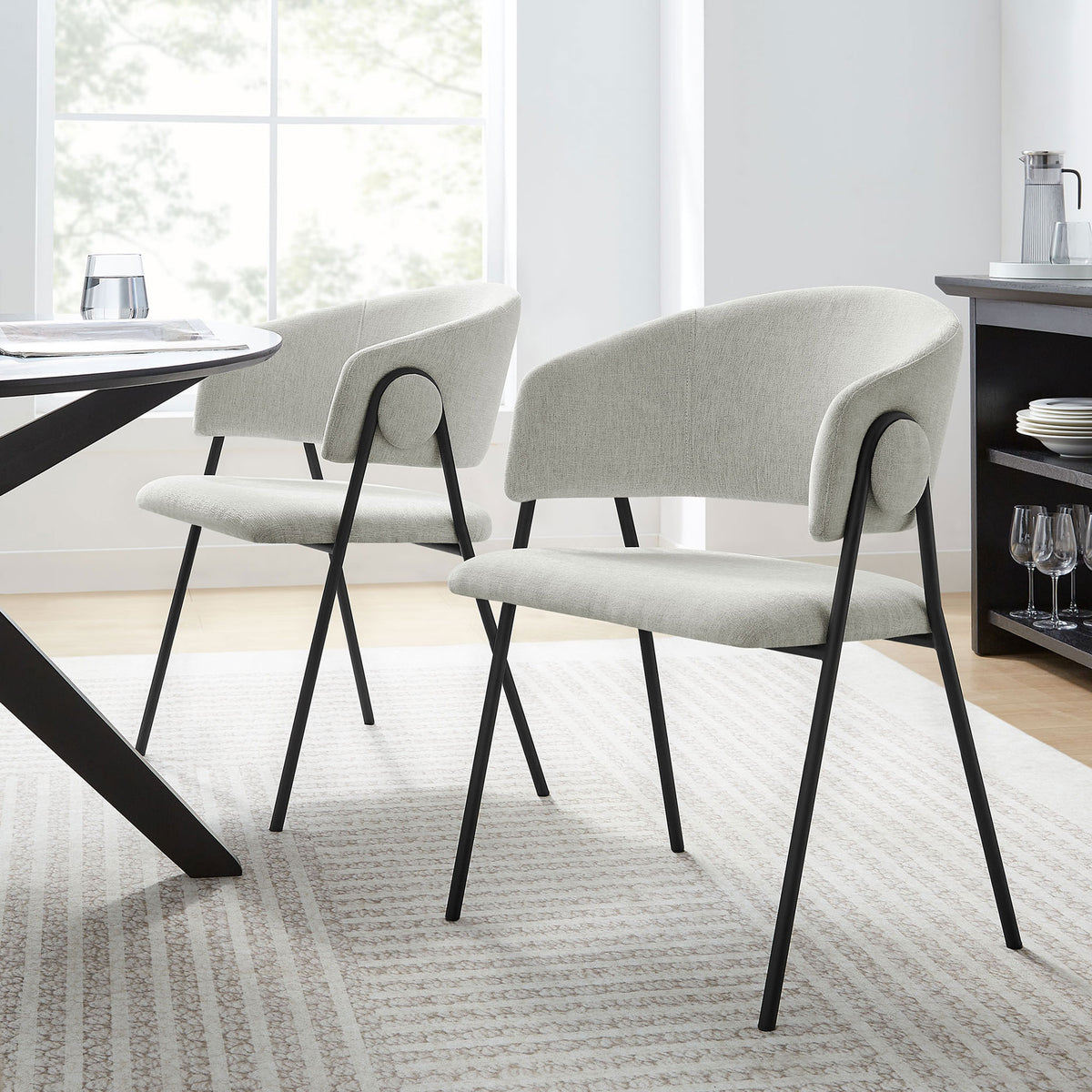 Pair of upholstered barrel dining chairs around a modern table in a bright, airy dining room || EEI-7045-NPT-BLK || front_angle_multi_room