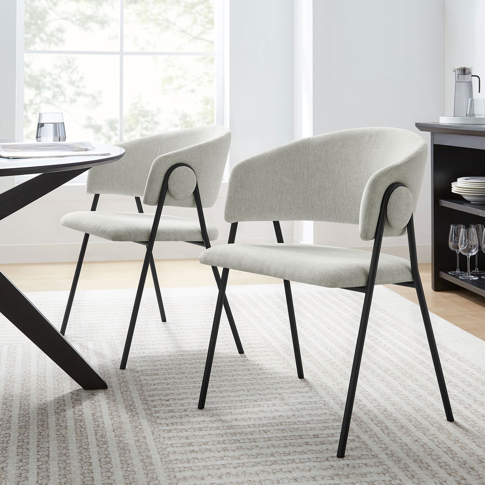 Pair of upholstered barrel dining chairs around a modern table in a bright, airy dining room || EEI-7045-NPT-BLK || front_angle_multi_room