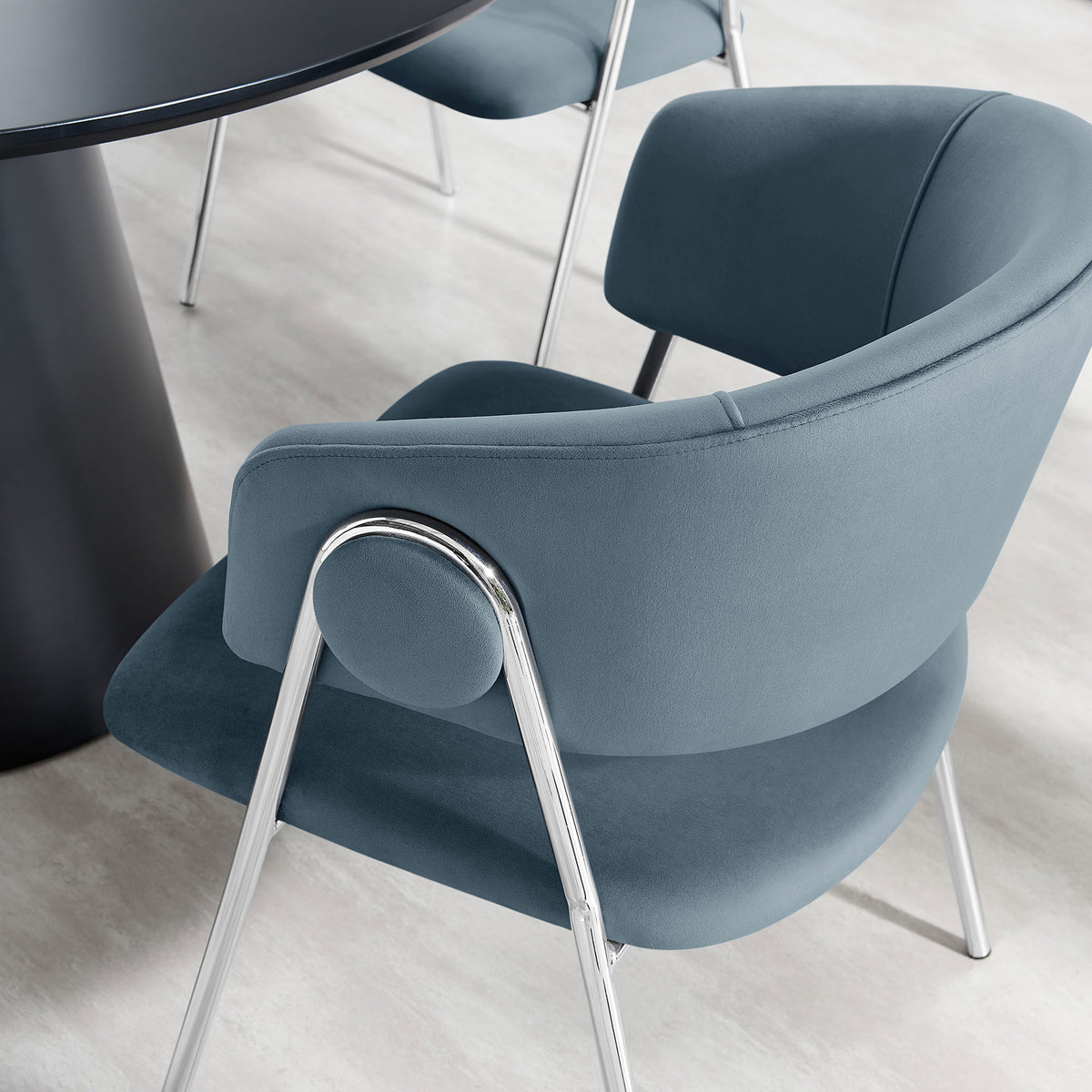 Cadet blue velvet dining chair tucked at a modern table, adding soft texture and curved comfort. || EEI-7046-CAD-SLV || front_angle_room