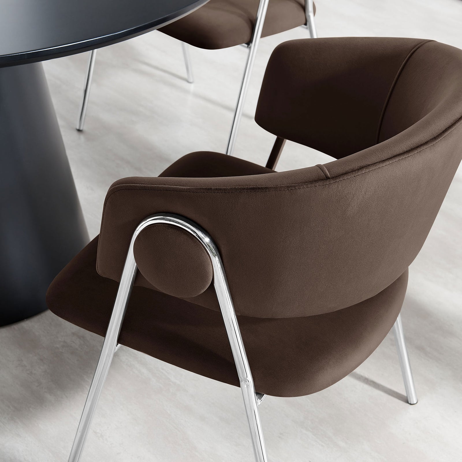 Nella dining chair in chocolate brown velvet tucked beside a sleek black table on a light contemporary floor. || EEI-7046-CHB-SLV || detail_room