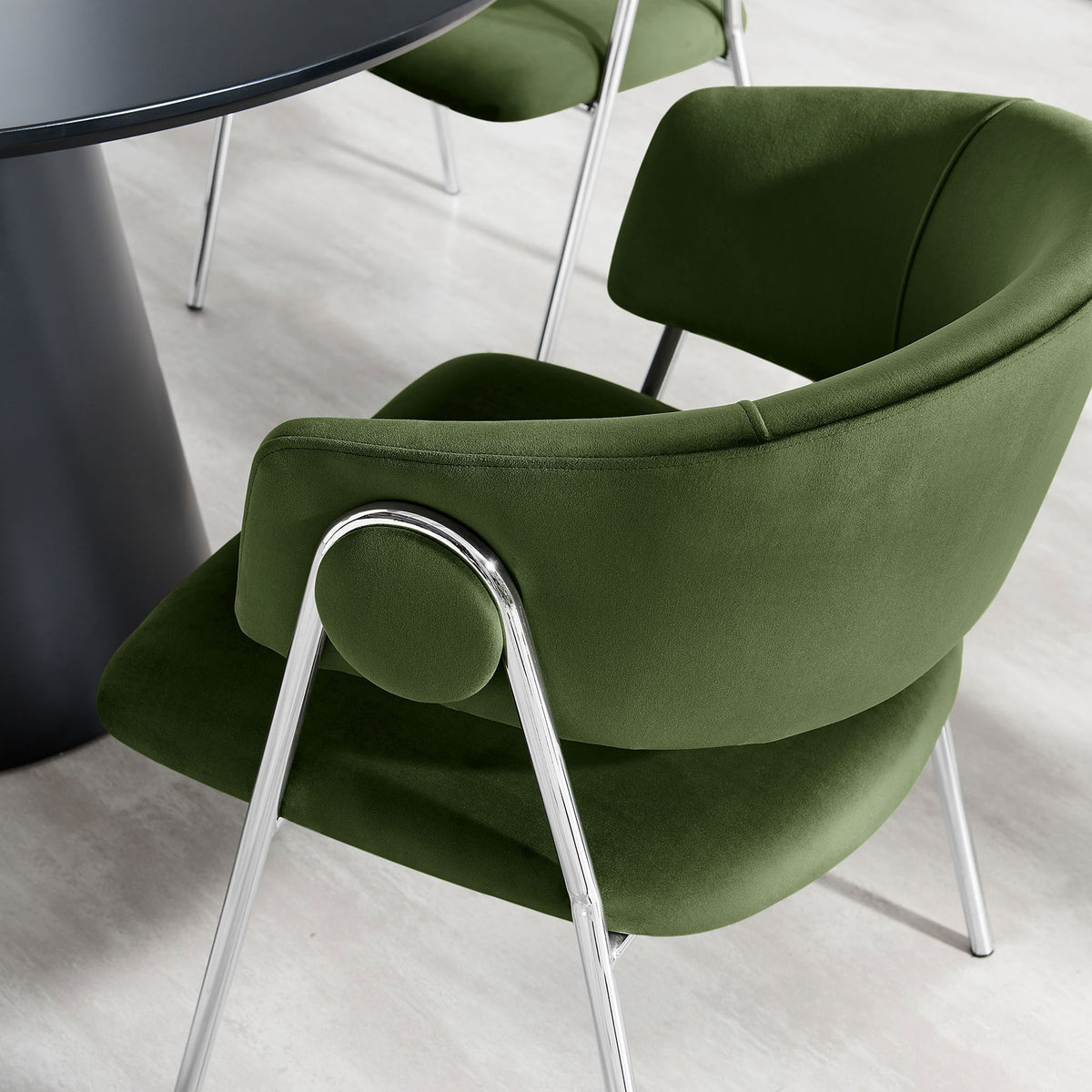 Velvet dining chair in moss green styled at a modern round table on a light floor || EEI-7046-MOG-SLV || front_angle_room