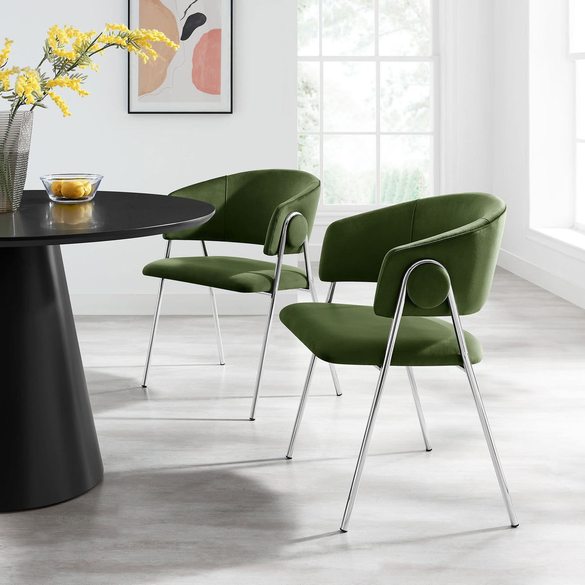 Set of two moss green velvet dining chairs arranged around a contemporary black pedestal table || EEI-7046-MOG-SLV || front_angle_multi_room