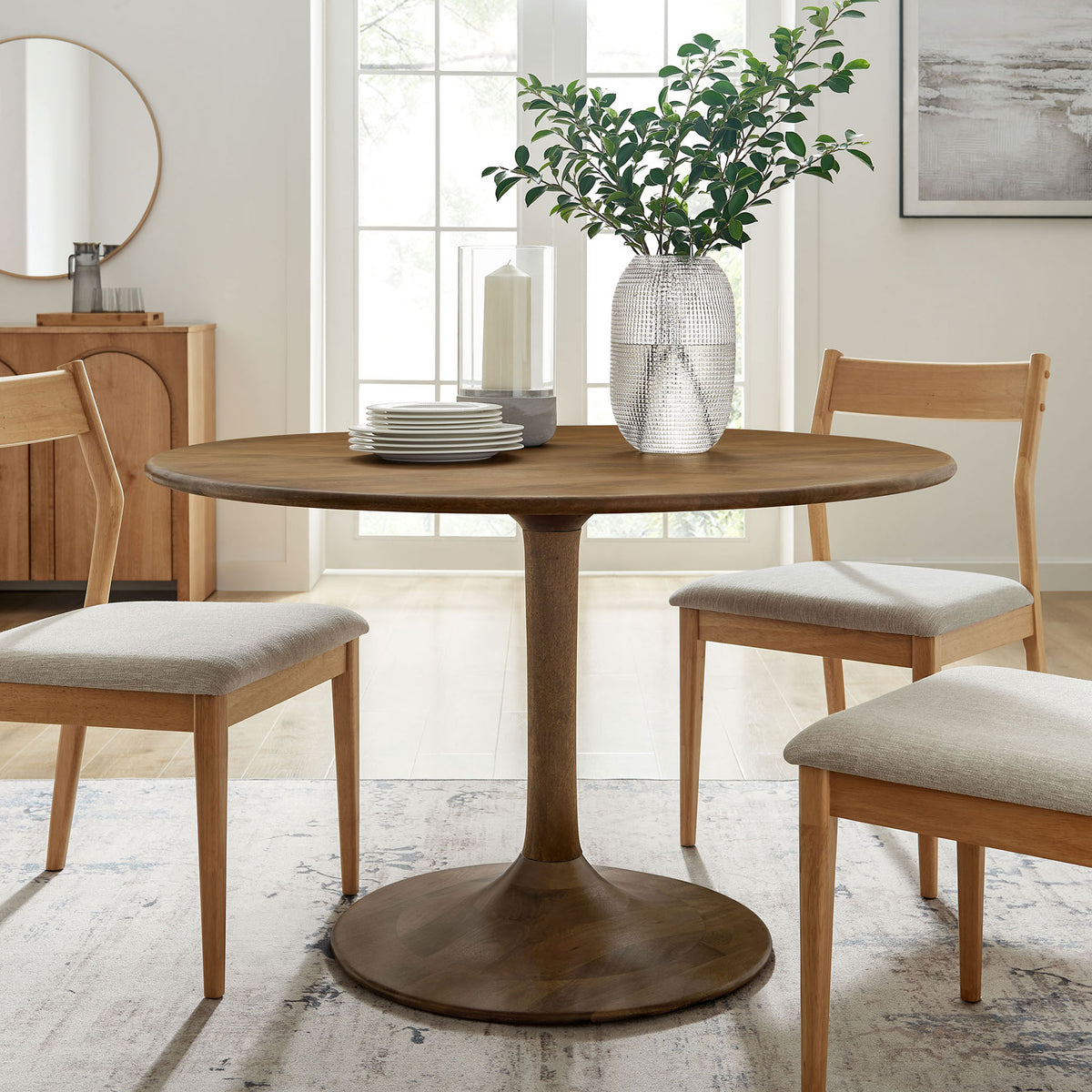 Round natural wood pedestal dining table styled with chairs in a bright modern dining room || EEI-7051-NAT || front_angle_room