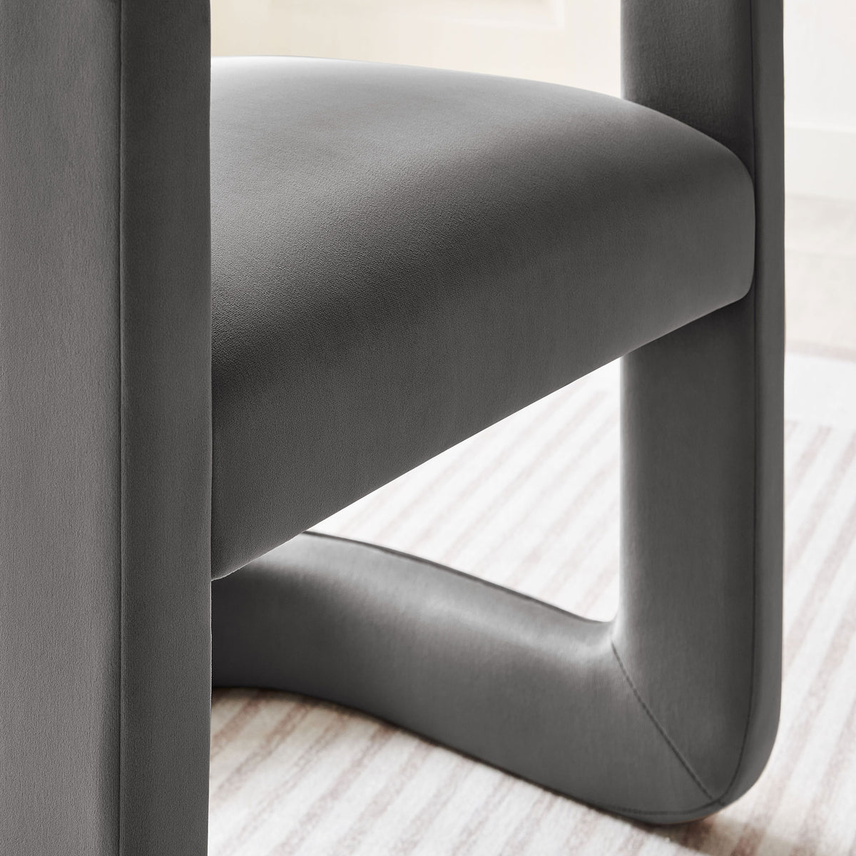 Storm gray velvet seat and sculpted base of the dining chair styled on a striped rug in a bright room. || EEI-7052-STG || detail_room