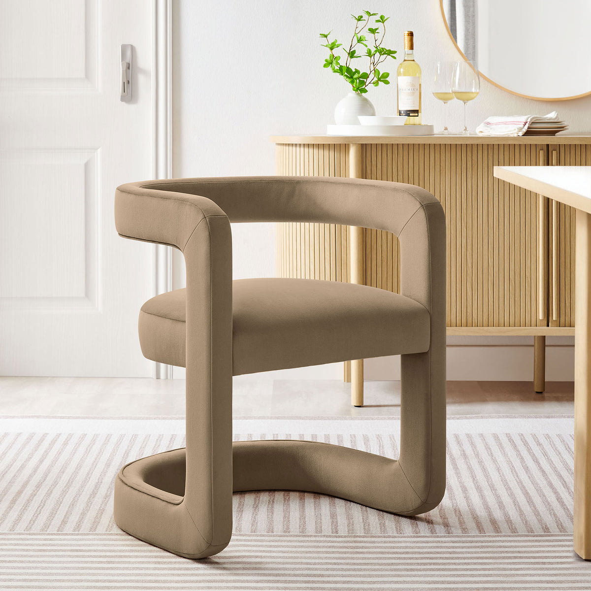 Taupe velvet barrel dining chair styled in a bright dining room beside a wood sideboard. || EEI-7052-TAU || front_angle_room