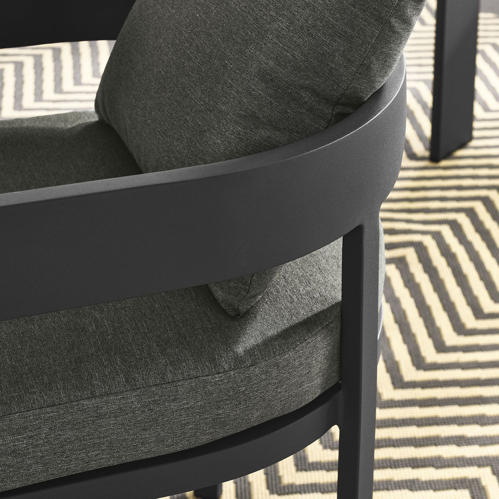 Detail of charcoal patio dining chair arm and cushions over a geometric outdoor rug by the table || EEI-7053-GRY-CHA || detail_room