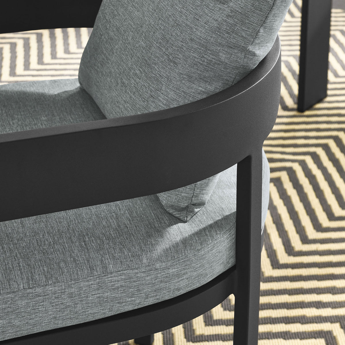 Detail of charcoal patio dining chair arm and gray cushions over a geometric outdoor rug by the table || EEI-7053-GRY-GRY || detail_room