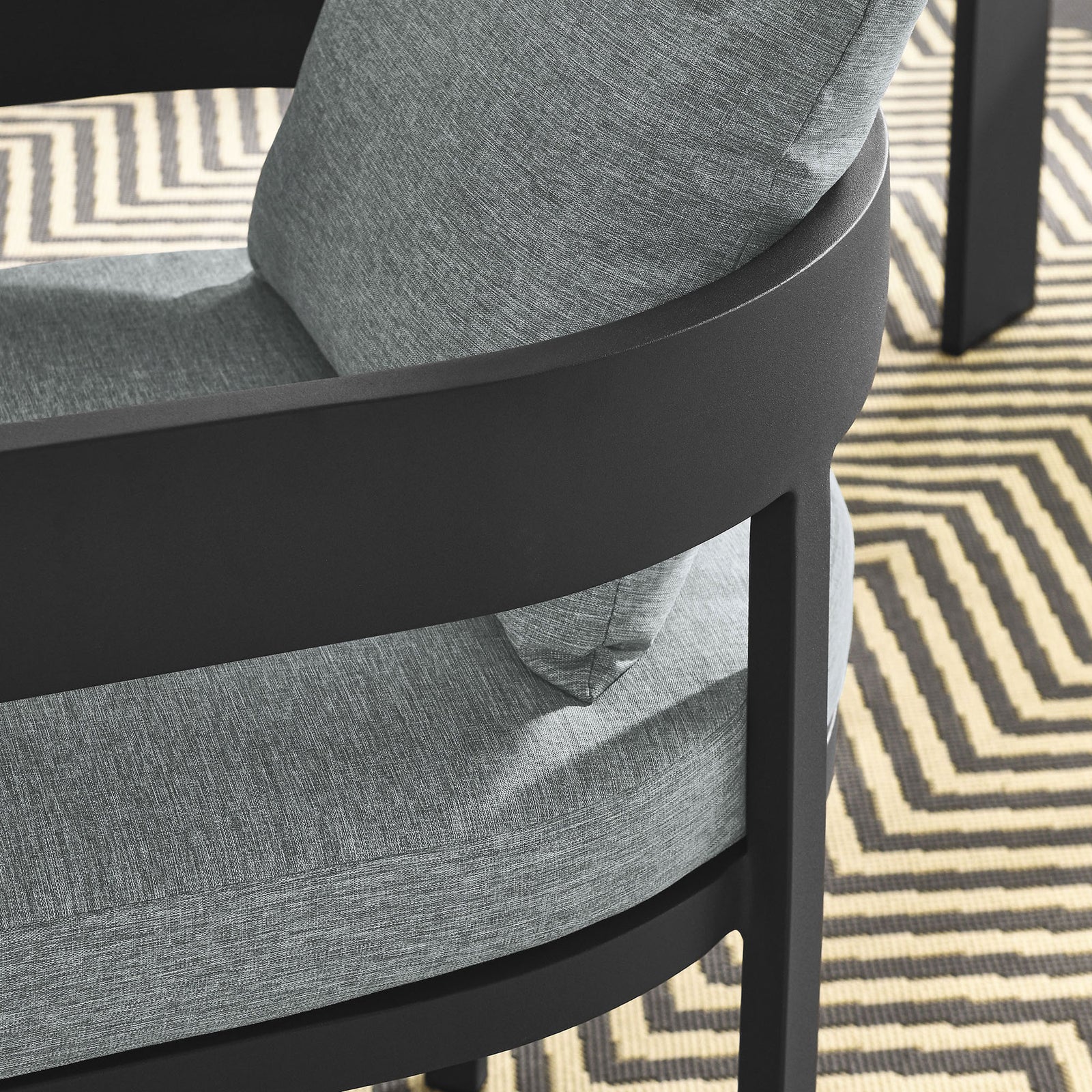Detail of charcoal patio dining chair arm and gray cushions over a geometric outdoor rug by the table || EEI-7053-GRY-GRY || detail_room