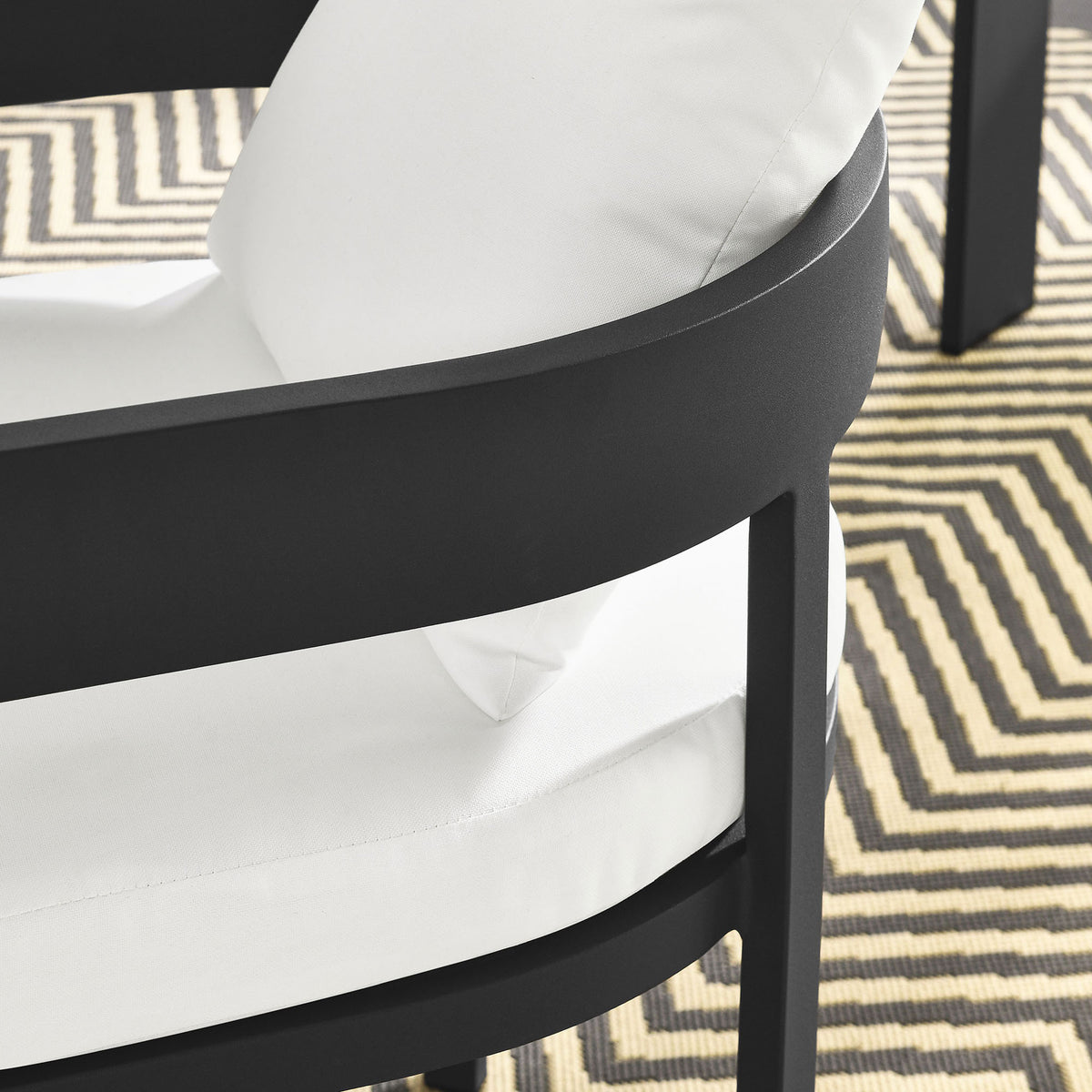 Detail of charcoal patio dining chair arm and white cushions over a geometric outdoor rug by the table || EEI-7053-GRY-WHI || detail_room