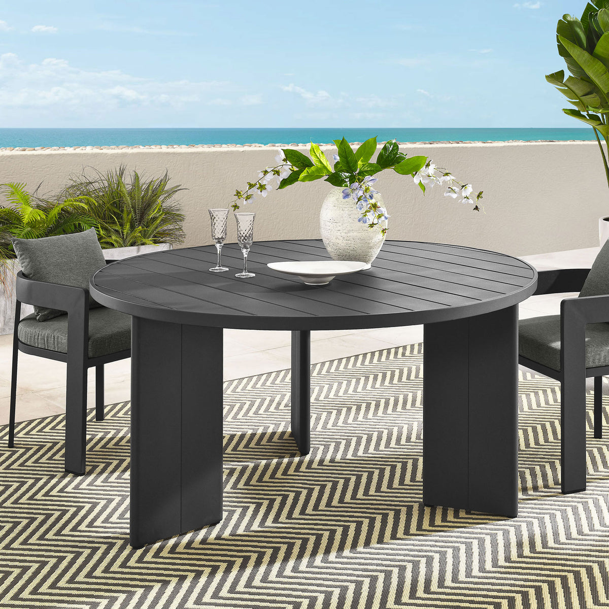 Tahoe round patio table styled with lounge chairs, rug, and greenery for relaxed outdoor dining. || EEI-7055-GRY || front_angle_room