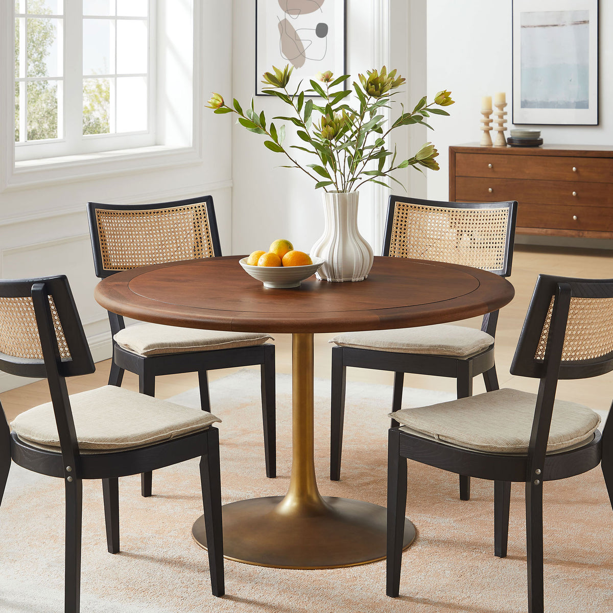 Round walnut pedestal dining table paired with modern chairs, creating a cozy, light-filled gathering space || EEI-7070-BRA-WAL || front_room
