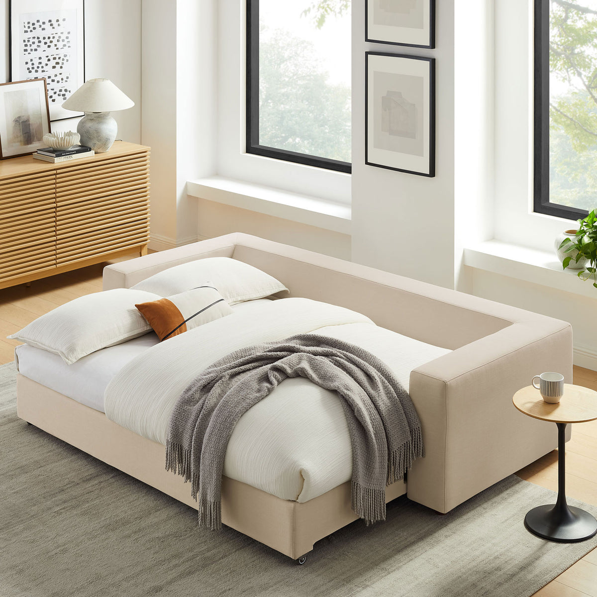 Sleeper sofa transformed into a plush full-size bed dressed in white linens and a soft gray throw || EEI-7080-LBG || front_angle_converted_room