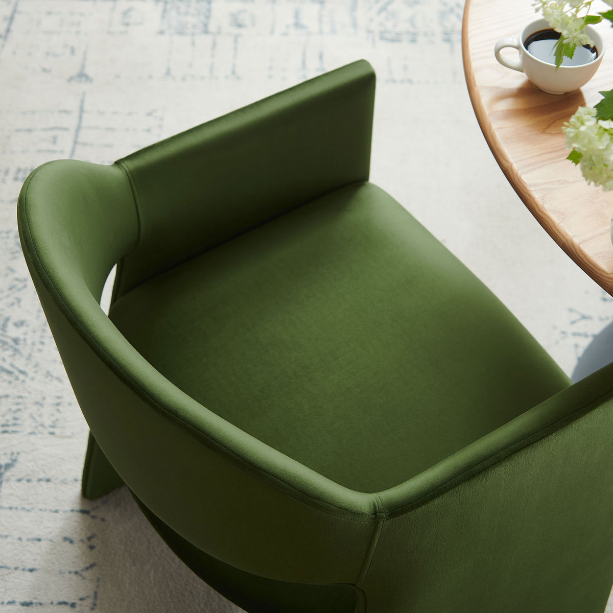 Moss green velvet barrel-back dining chair pulled up to a round table, revealing the curved back and roomy seat. || EEI-7081-MOG || detail_room
