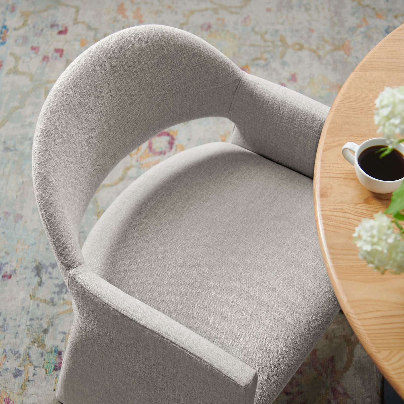 Talia dining armchair in linen tucked under a round wood table on a softly patterned rug. || EEI-7082-LIN || detail_room