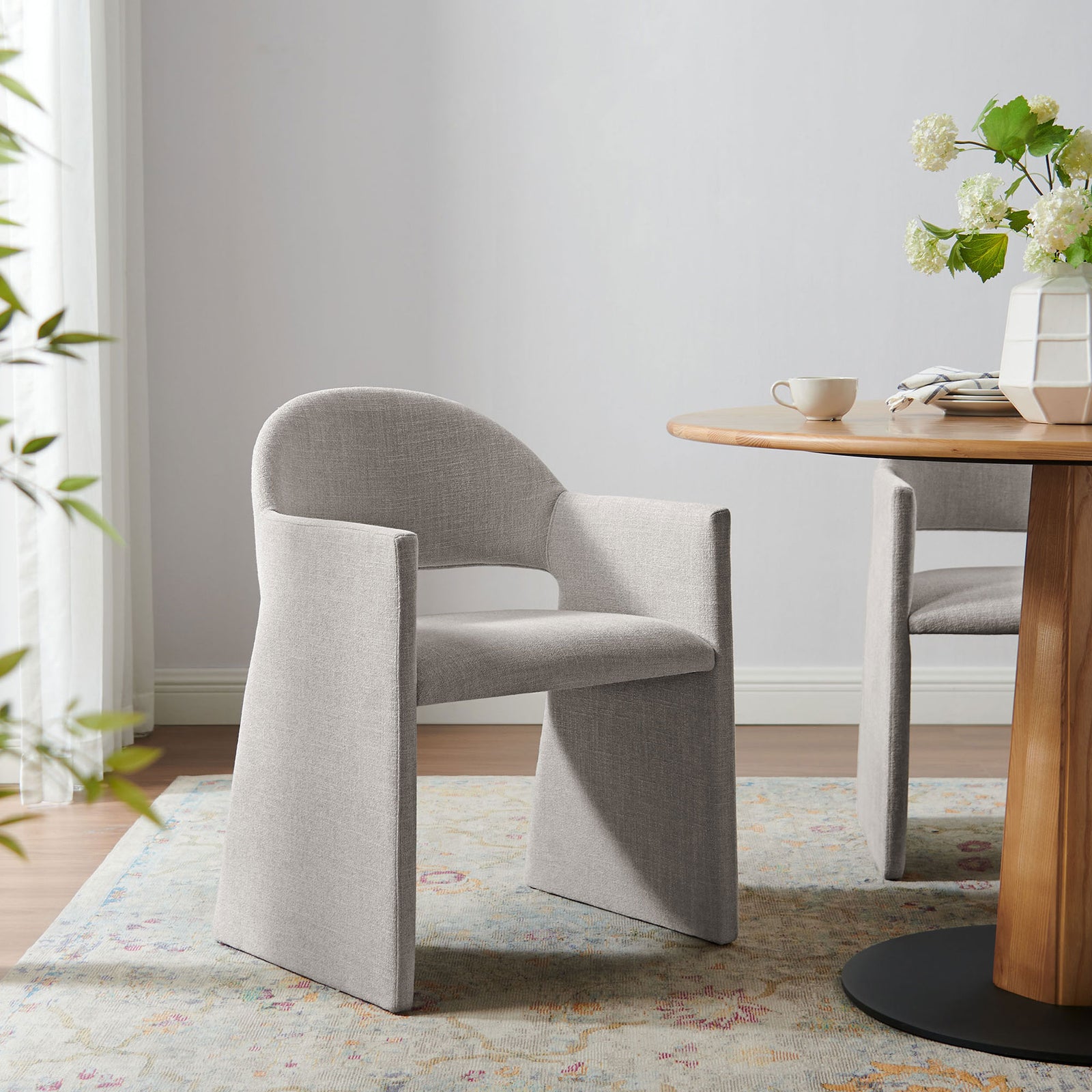 Linen upholstered Talia dining armchair styled in a bright dining room with wood table and floral accents. || EEI-7082-LIN || front_angle_room