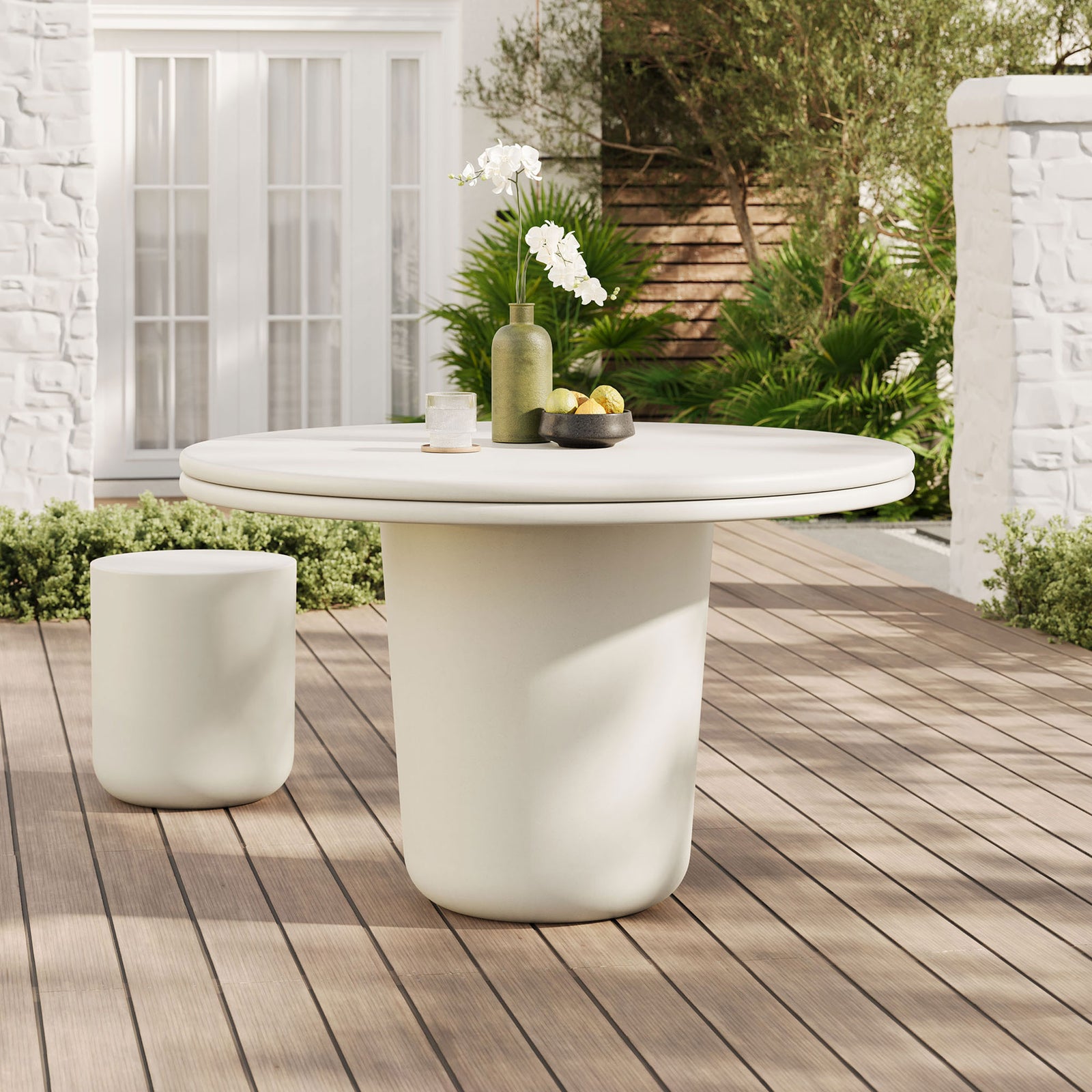 White concrete round dining table on a wood deck patio with matching accent stool and greenery || EEI-7087-WHI || front_angle_room