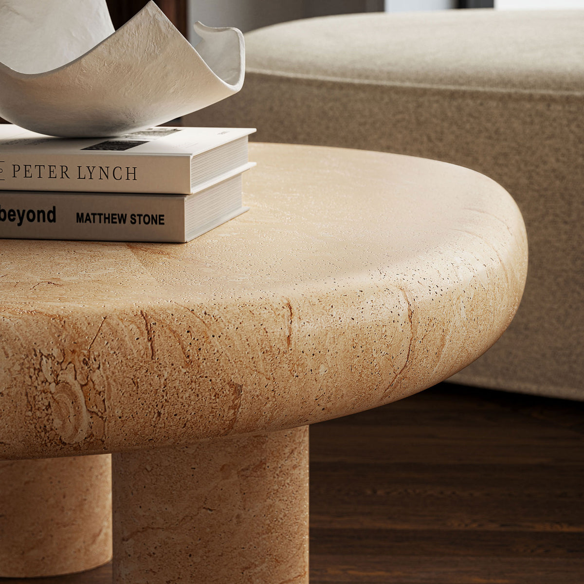 Kidney-shaped faux travertine table adds sculptural texture beside a plush indoor chair and stacked books || EEI-7093-TRV || detail_room