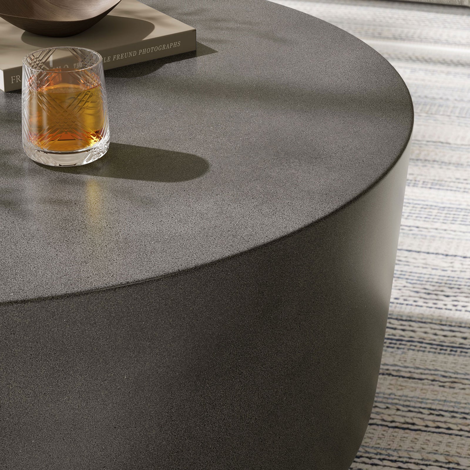 Detail of the gray concrete coffee table surface with a drink, highlighting its smooth rounded edge || EEI-7099-GRY || detail_room