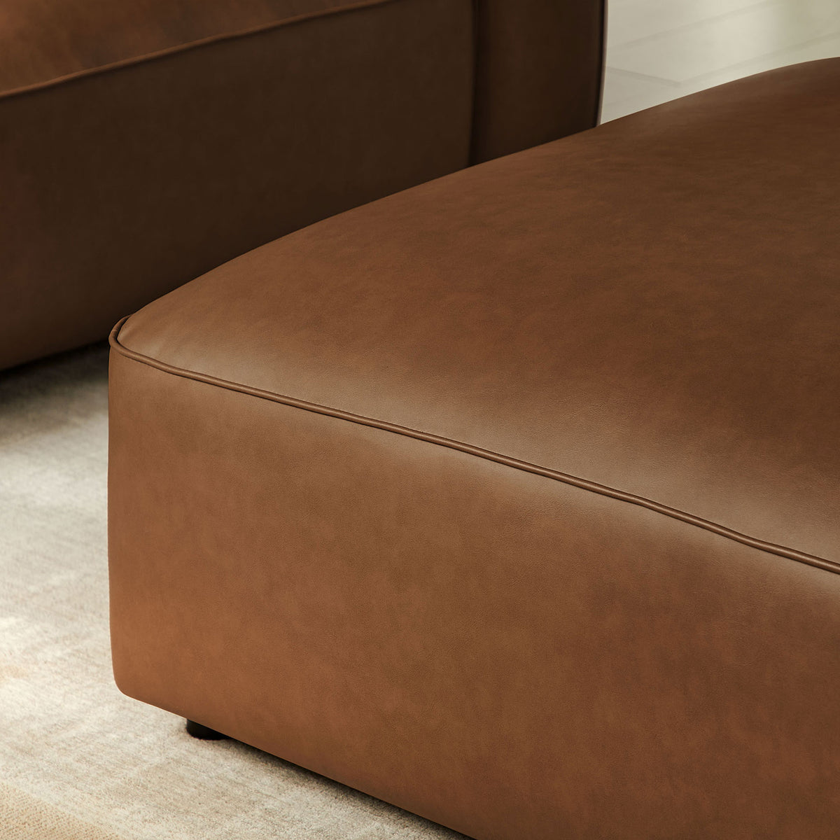 Detail of coffee vegan leather ottoman in a living room, highlighting tailored seams and plush padding || EEI-7125-COF || detail_room