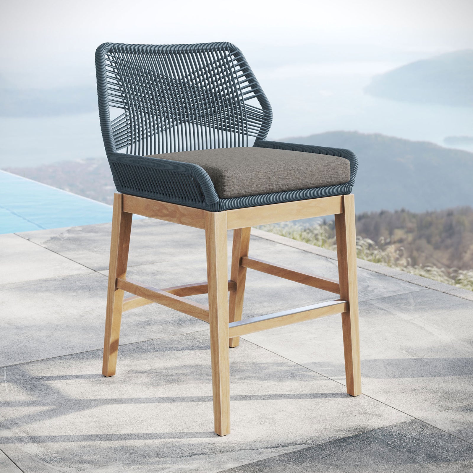 Blue graphite rope counter stool with gray cushion and teak legs styled on a terrace overlooking the water. || EEI-7126-BLU-GPH || front_angle_room