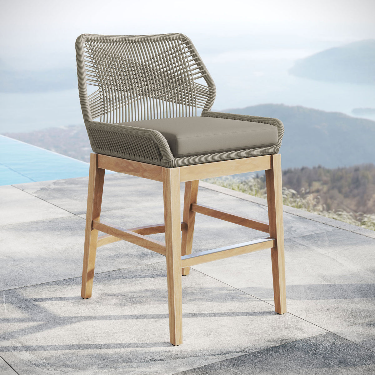 Light gray greige rope counter stool with cushion and teak legs styled by a poolside terrace and open vista. || EEI-7126-LGR-GRG || front_angle_room