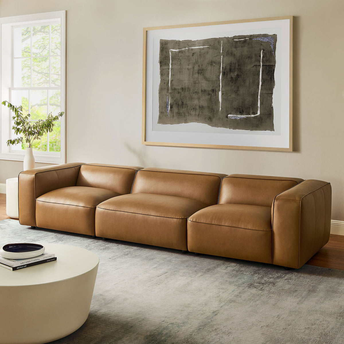 Camel Auren modular sofa styled in a bright living room with oversized artwork and a round coffee table || EEI-7132-CAM || front_angle_room