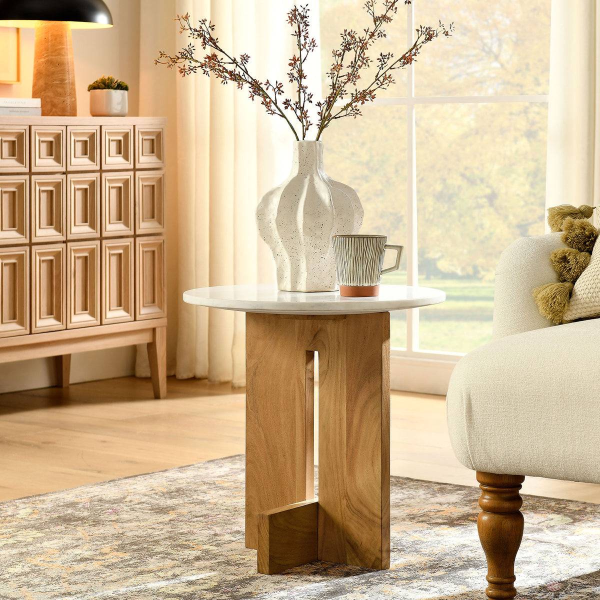 Round marble side table adding modern warmth beside a cozy sofa in a bright living room || EEI-7141-NAT || front_angle_room