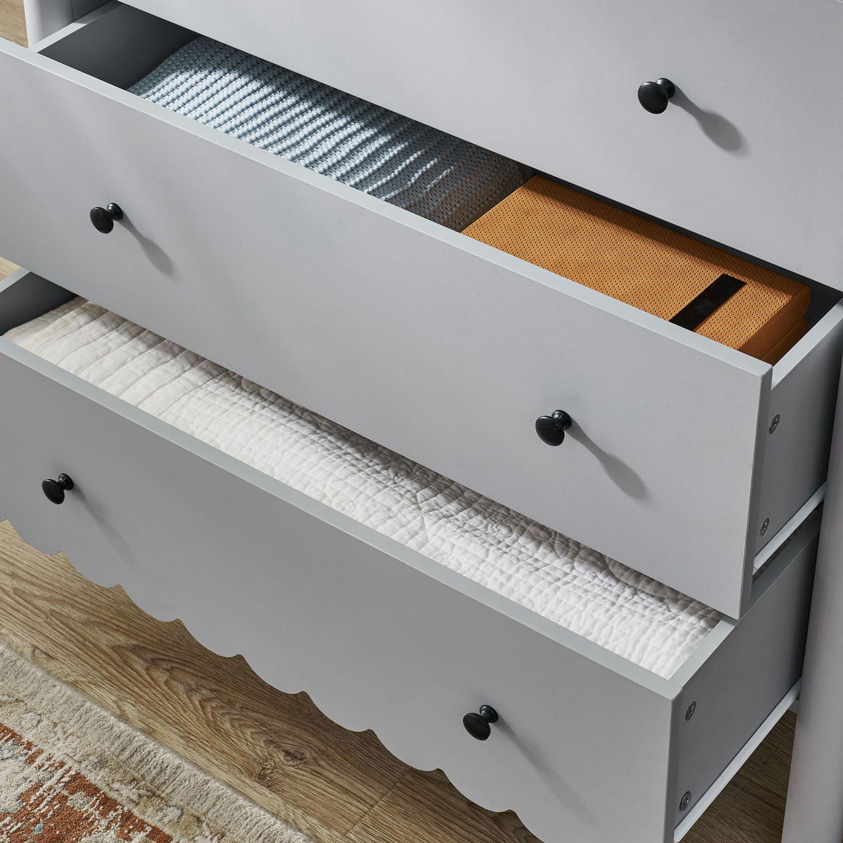 Drawers filled with blankets and boxes inside the scalloped chest beside a rug || EEI-7156-LGR || storage_open_room