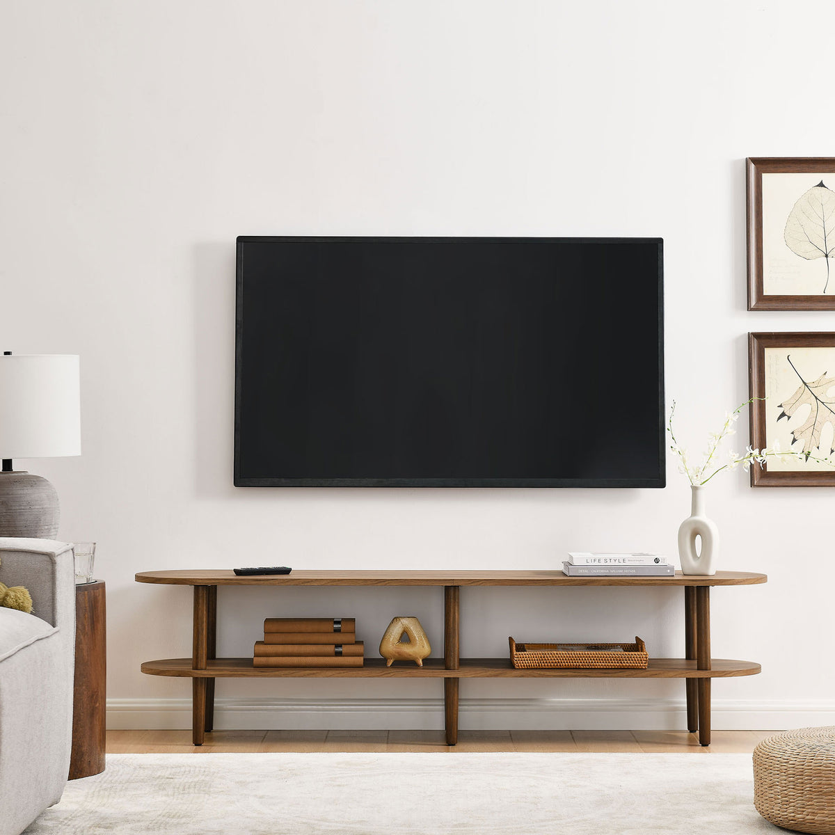 Walnut oval TV stand grounding a modern living room beneath a wall mounted flat screen TV || EEI-7158-WAL || front_room