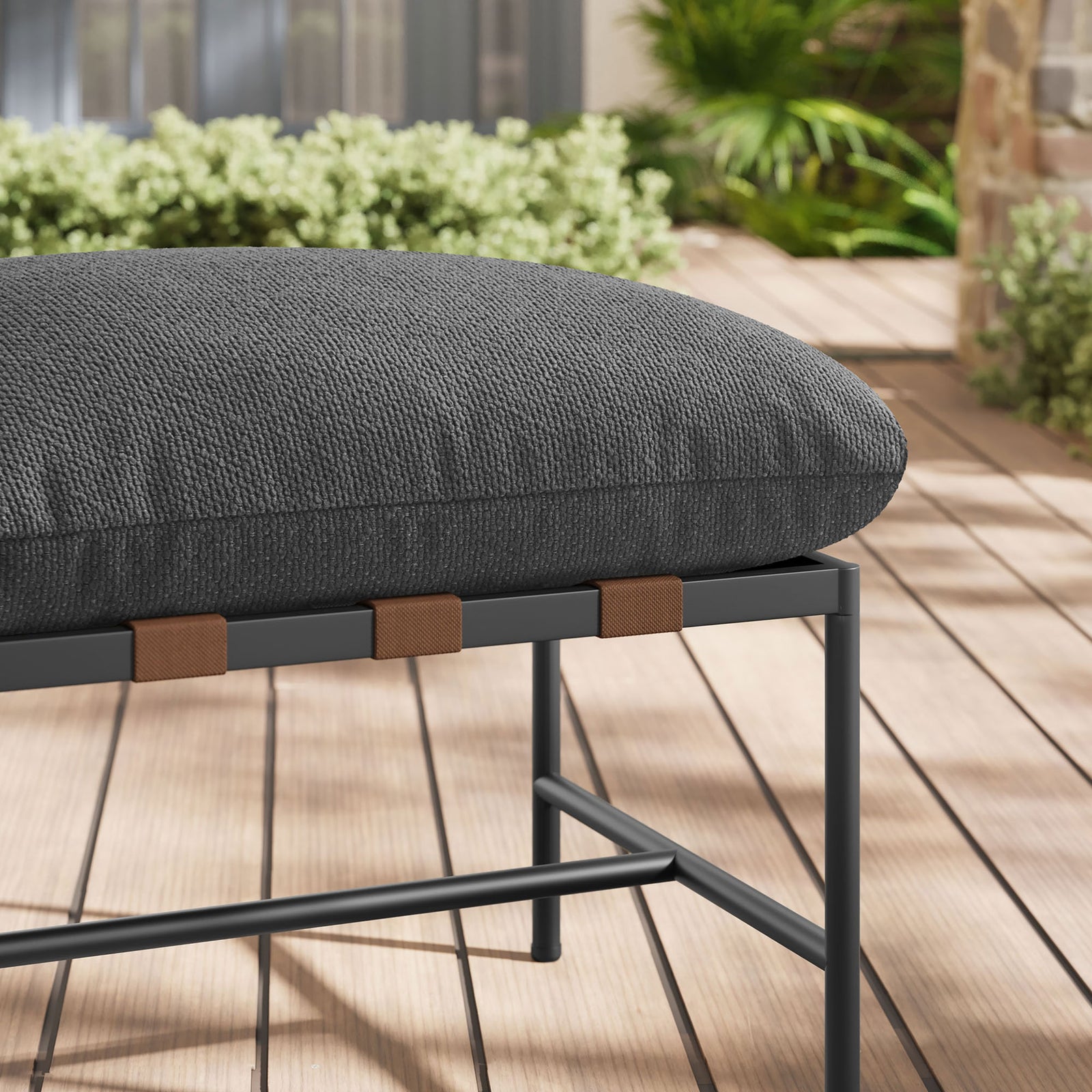 Charcoal boucle cushion and strap detailing of the outdoor ottoman layered over warm wood decking and greenery || EEI-7161-CHA || detail_room