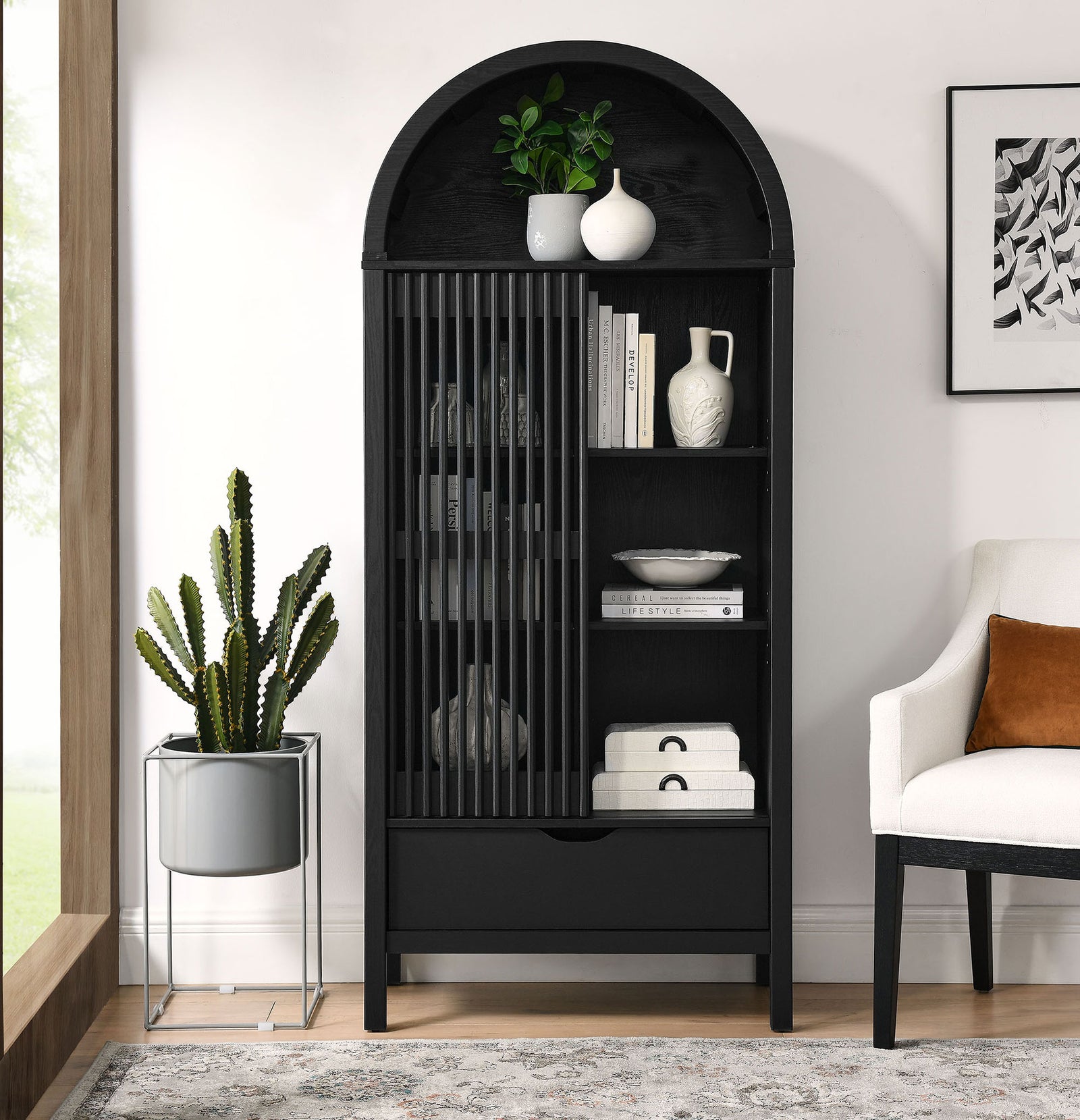 Black arched display cabinet styled in a living room with decor arranged behind the slatted door. || EEI-7167-BLK || front_open_room