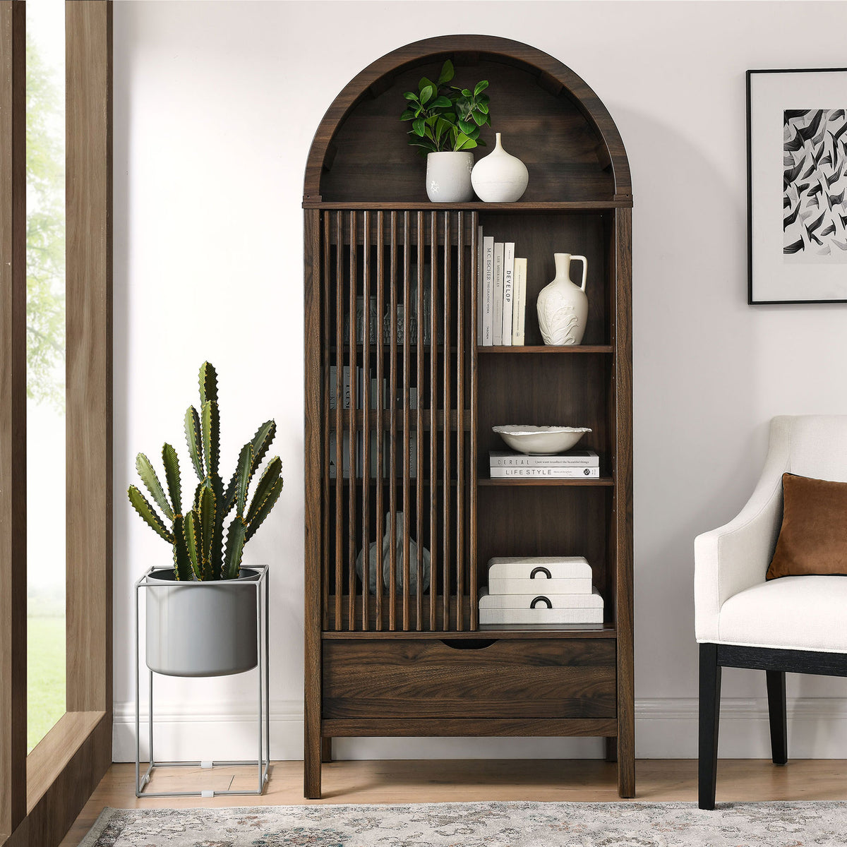 Walnut arched display cabinet styled in a living room with decor arranged behind the slatted door. || EEI-7167-WAL || front_open_room