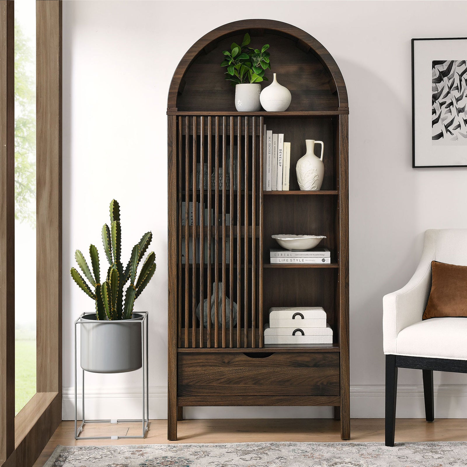 Walnut arched display cabinet styled in a living room with decor arranged behind the slatted door. || EEI-7167-WAL || front_open_room